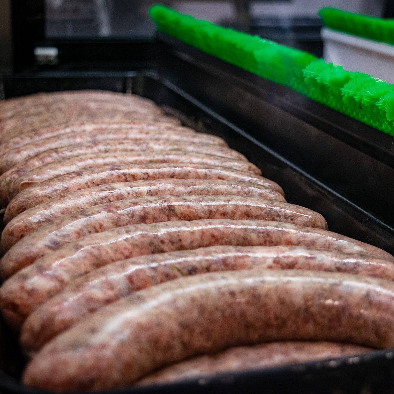 Row of raw sausages on a black tray with green packaging material in the background.