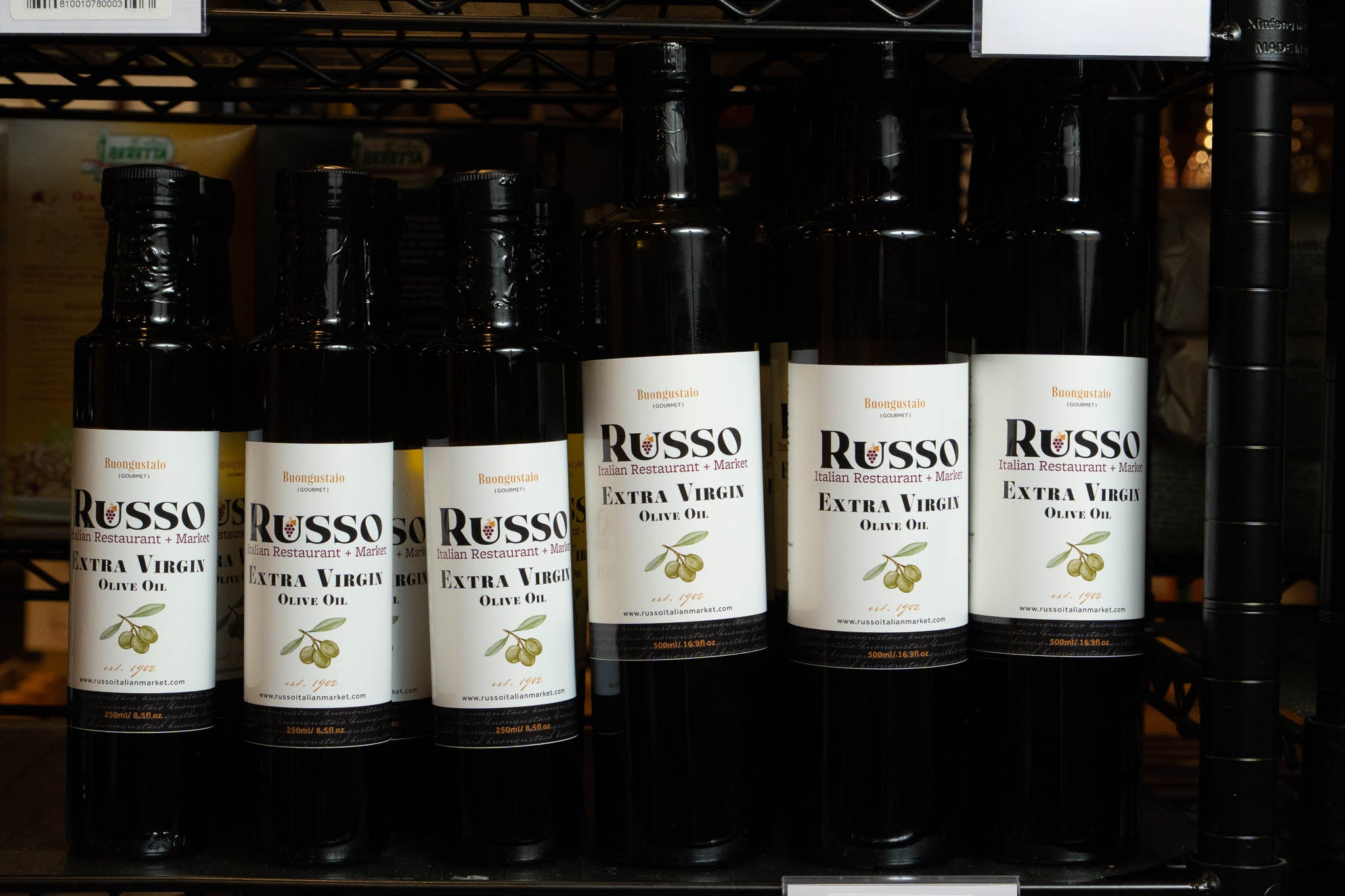 Row of Russo olive oil bottles with labels on a metal rack.